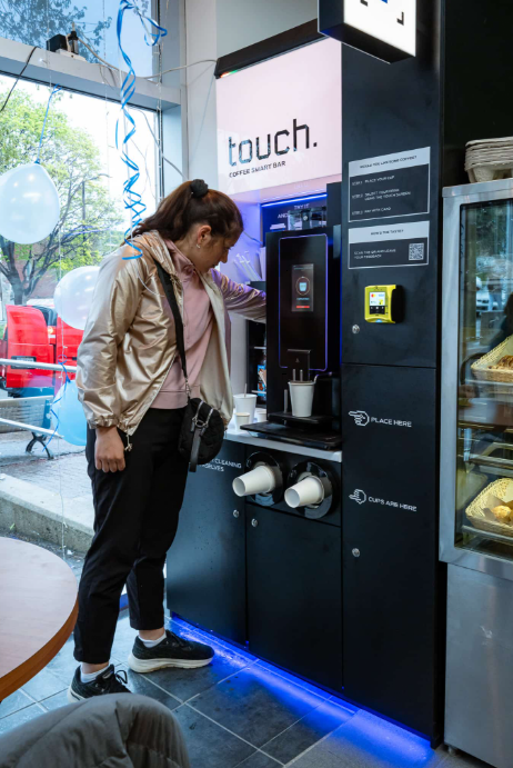 A guest ordering at our Touch Coffee smart bar, with the screen, cup station, and payment reader.